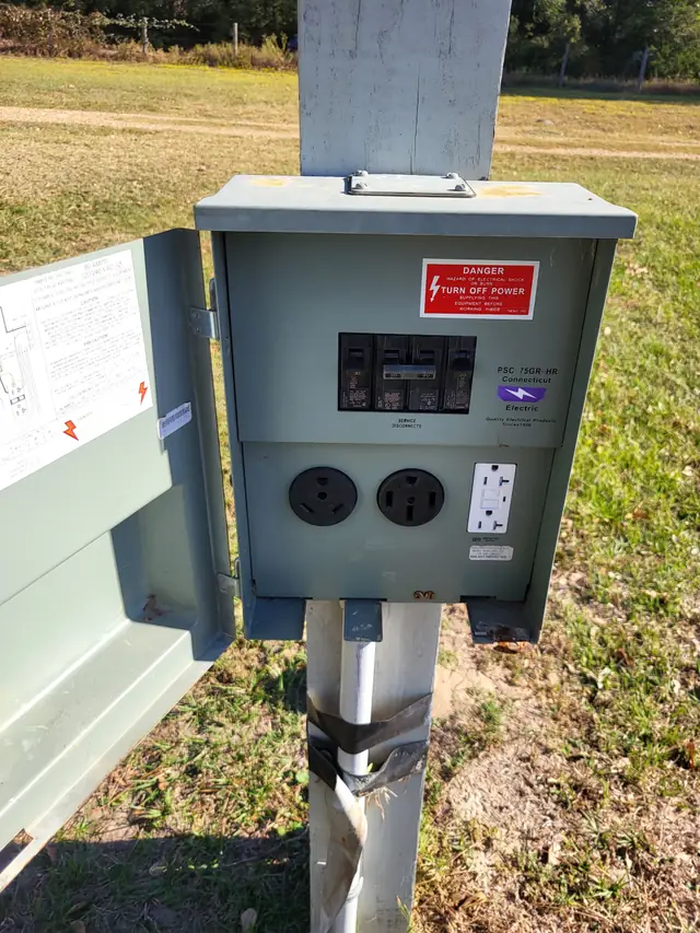 A site's power pedestal on a post: two RV outlets for 30 and 50 amp service and a GFCI outlet, grass behind